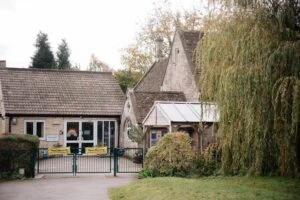 The entrance to the village primary school, with stone buildings, a green gate and a weeping willow